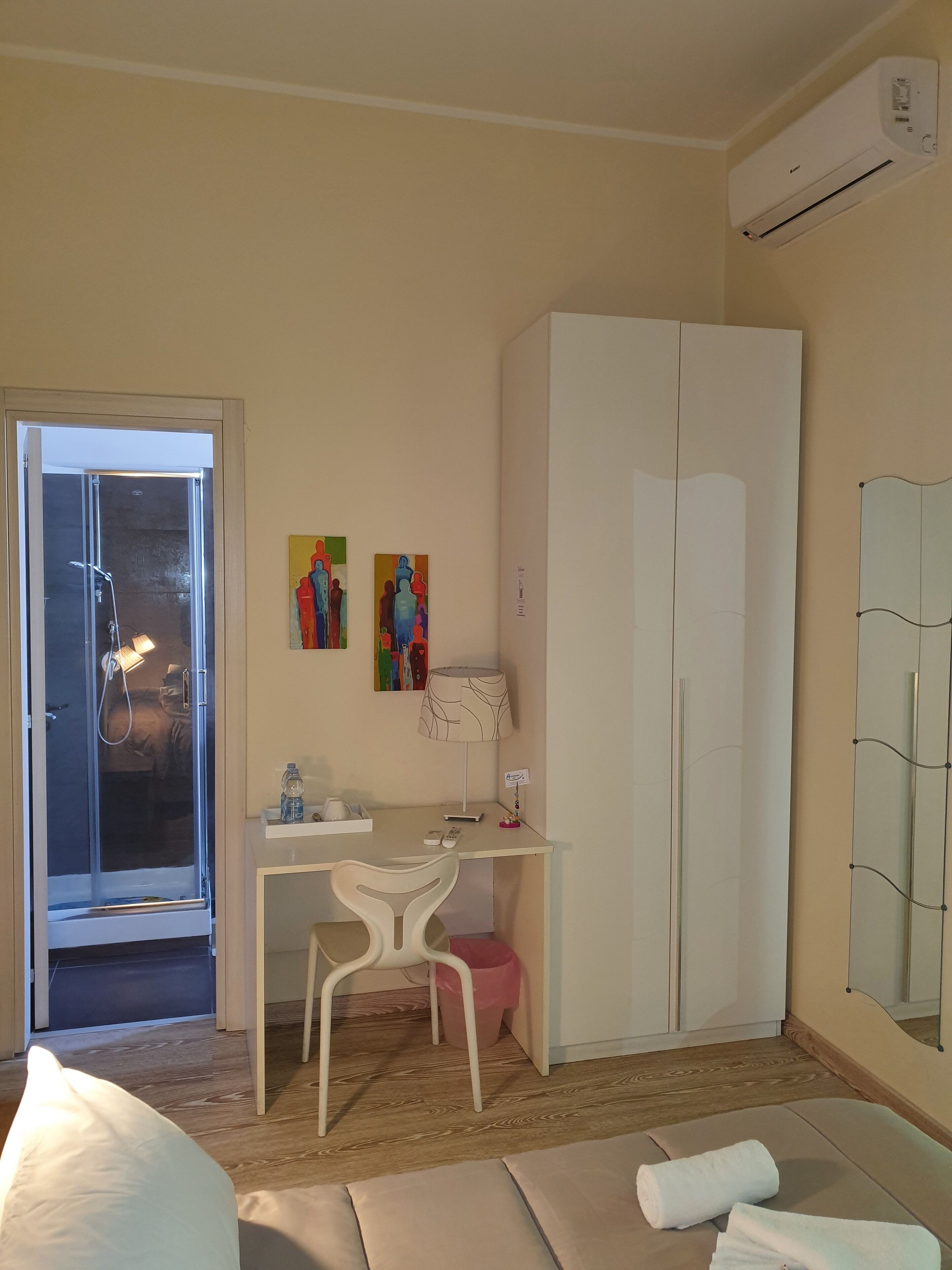 Ein Zimmer mit einem Bett, einem Schreibtisch, einem Stuhl, einem Kleiderschrank, einer Dusche und zwei Bildern an der Wand.