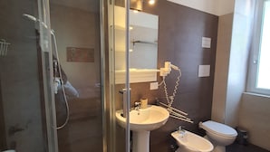 Un baño moderno con ducha de vidrio, lavamanos pedestal, un bidé y un inodoro.