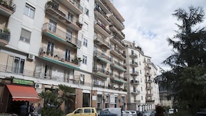 Un edificio residencial de varios pisos con balcones, coches aparcados y un peatón en la acera.