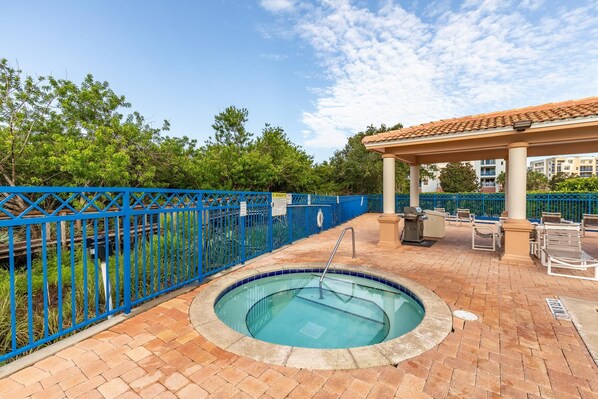 A pool area with a blue fence, a covered seating area, and a tiled patio.