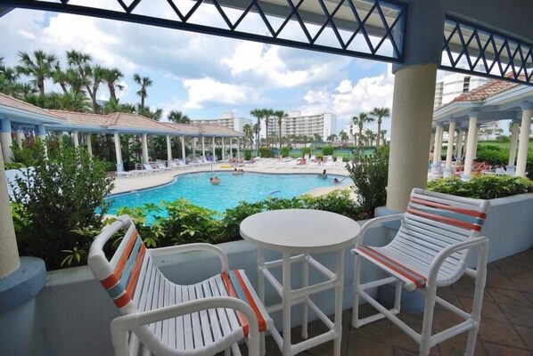 A poolside area with lounge chairs and a table, overlooking a swimming pool with people in the water. - Oceanwalk 20-205 (New Smyrna Beach)