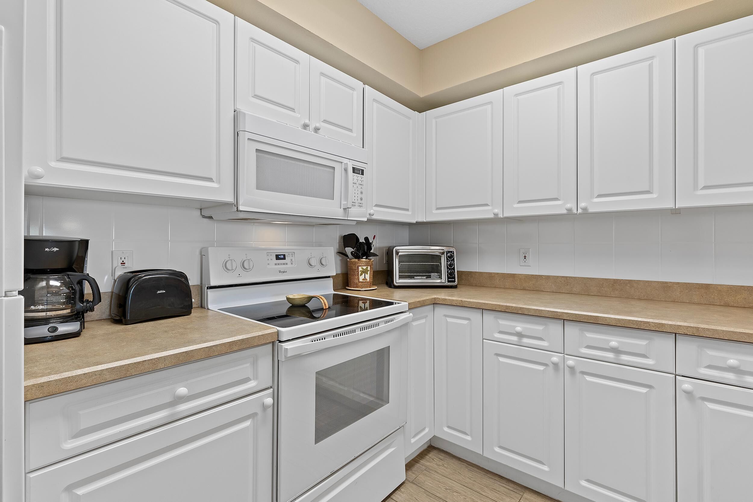 A kitchen with white cabinets, a microwave, a toaster, a coffee maker, and a stove.