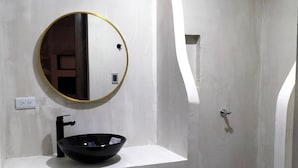 Un baño con un lavabo negro tipo recipiente, un espejo redondo con marco dorado y un mueble de tocador blanco.