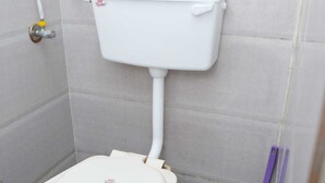 A white toilet with a tank and seat, a red bucket, and a purple cleaning tool in a tiled bathroom. - B type Cottage (Koroli)