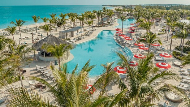 Een resort met een groot zwembad, palmbomen en ligbedden.
