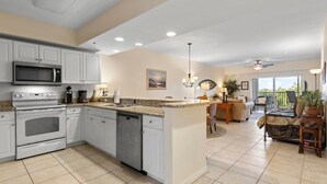 A spacious kitchen with white cabinets, a built-in microwave, and a dishwasher. There is a dining area with a table and chairs, and a large window offering a view of the outdoors.