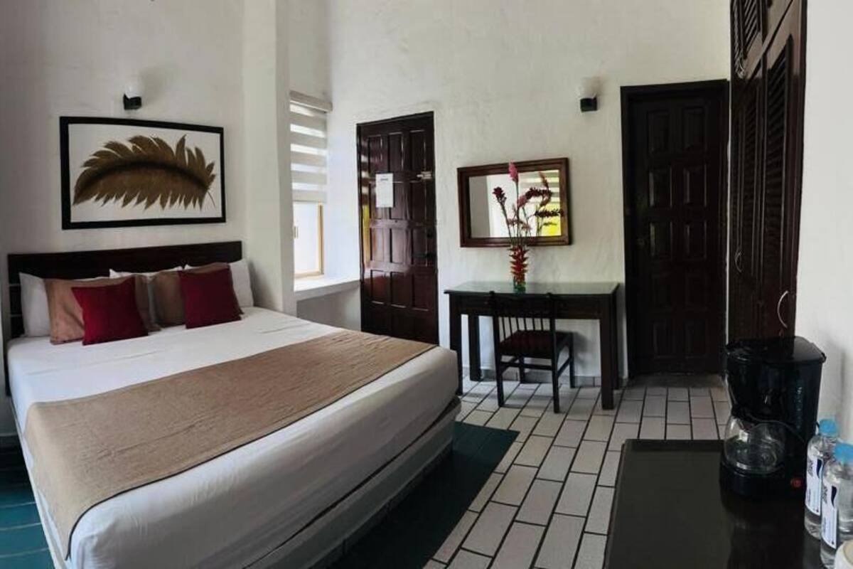 Habitación de hotel con cama, escritorio, silla, mesita y ventana con persianas.