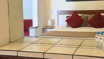 A bathroom with a tiled vanity, wooden drawers, a mirror, and a bed with red pillows in the background.