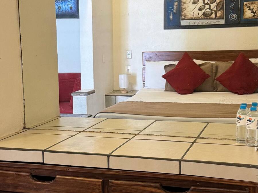 A bathroom with a tiled vanity, wooden drawers, a mirror, and a bed with red pillows in the background.