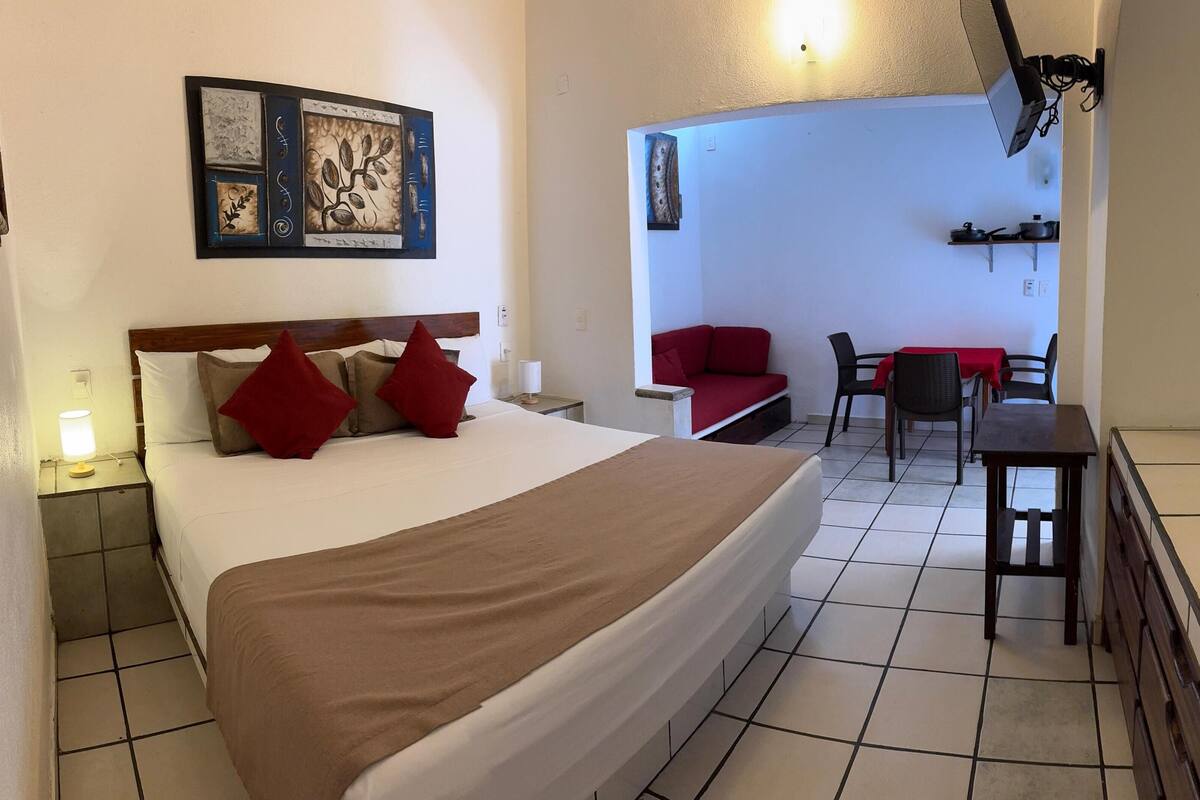Habitación de hotel con cama, escritorio, sillón, sofá y televisor montado en la pared.