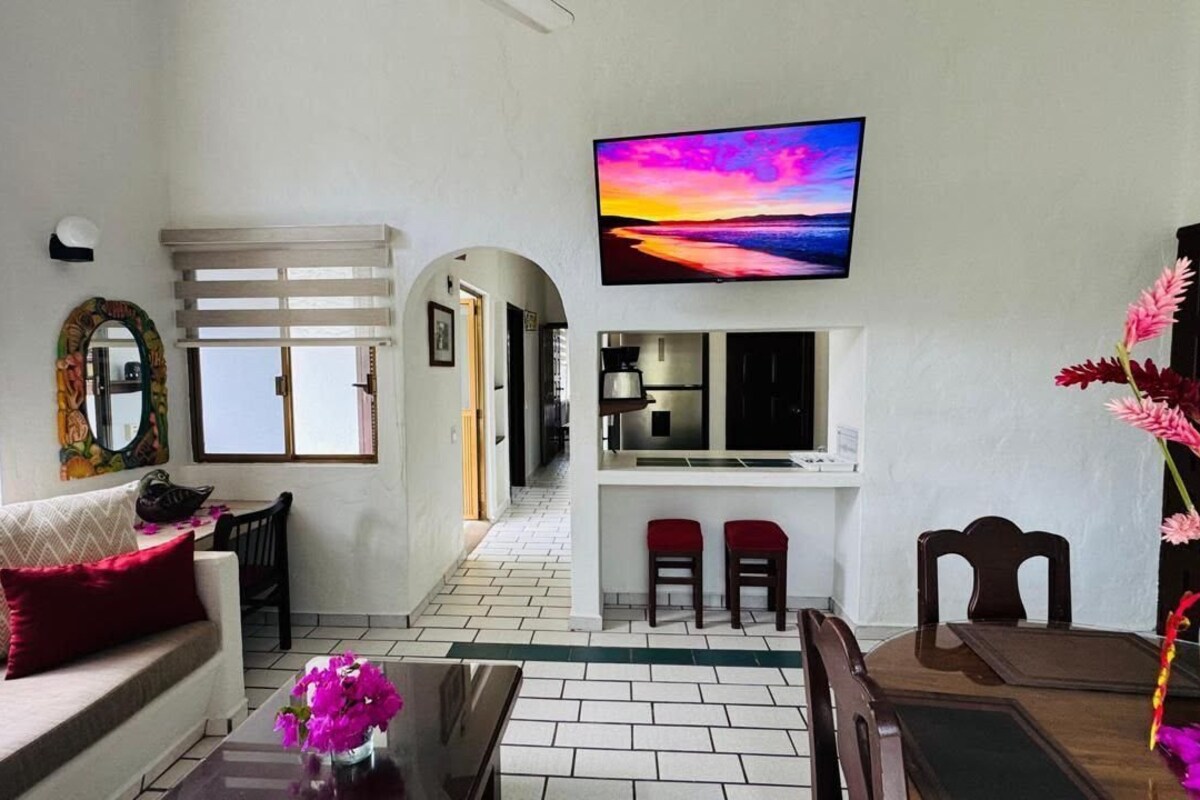 A living room with a sofa, coffee table, TV, and a dining area with chairs.