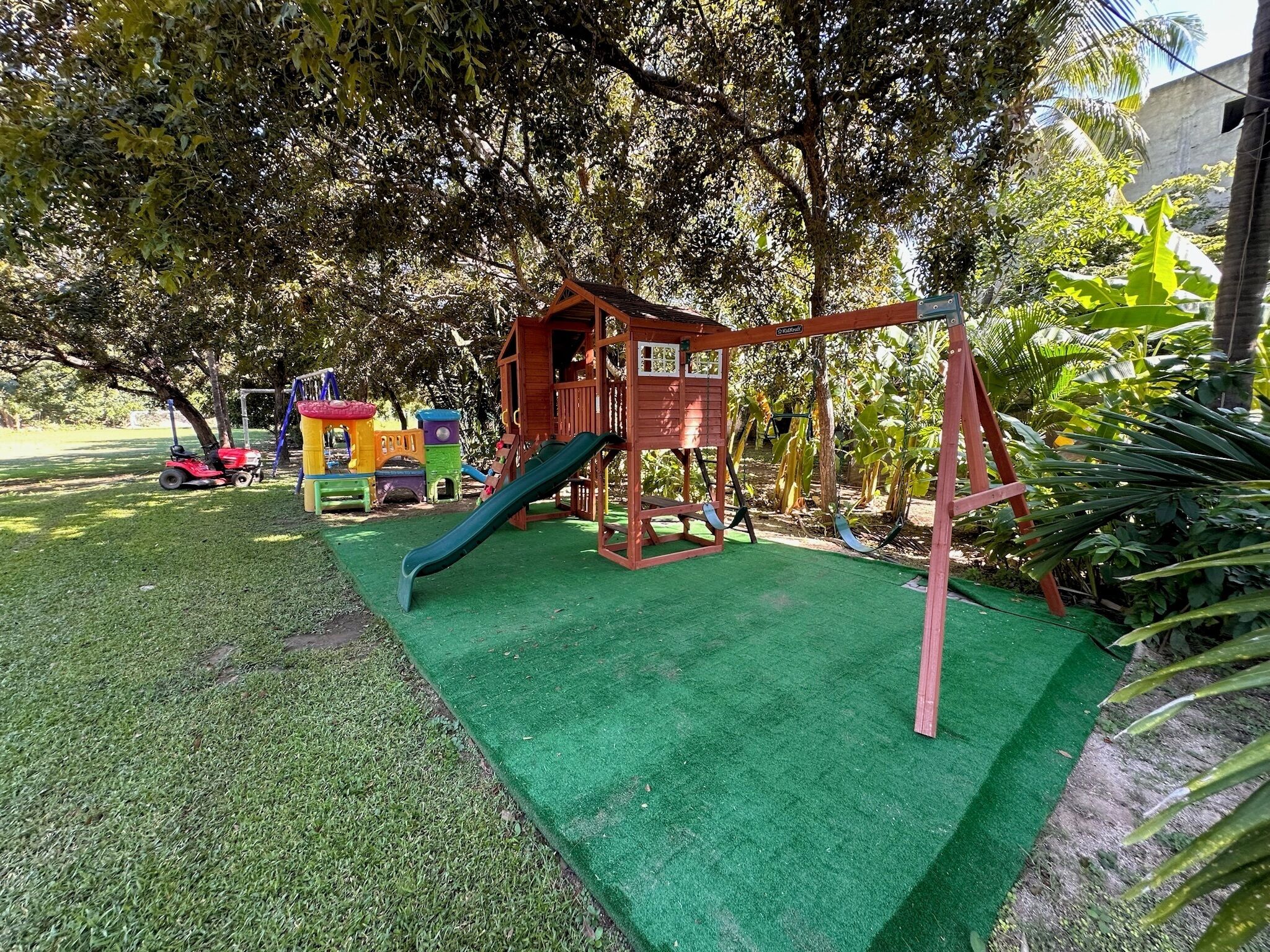 Un parque infantil con tobogán, columpios y una pequeña estructura de madera.