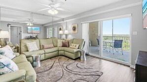 A modern living room with a sectional sofa, a ceiling fan, and a view of the balcony.