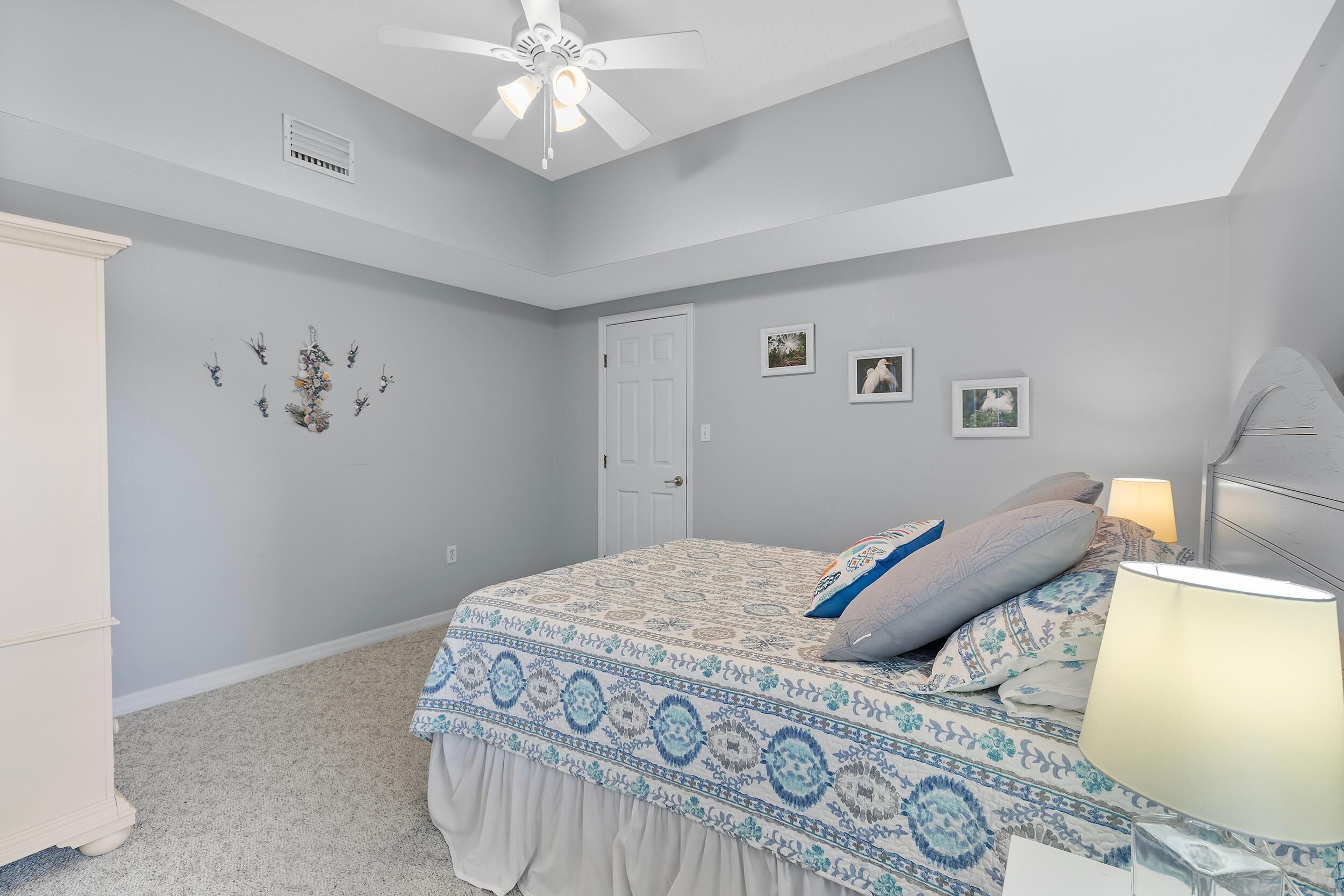 A bedroom with a bed, a ceiling fan, a door, and wall decorations.