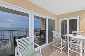 A balcony with white chairs and a table, overlooking a body of water. - Ponce de Leon Towers 303 (New Smyrna Beach)