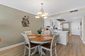 A dining area with a wooden table, white chairs, and a chandelier. - Ponce de Leon Towers 303 (New Smyrna Beach)