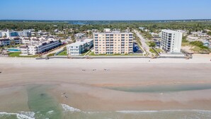 Un hotel frente a la playa con varias edificaciones, una playa arenosa y vista al océano.