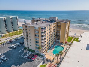 A multi-story hotel with a rooftop pool, a parking lot, and a beach view. - Ponce de Leon Towers 303 (New Smyrna Beach)