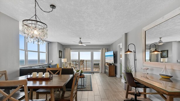 A spacious living area with a dining table, chairs, a chandelier, and a large window overlooking the ocean. - Ponce de Leon Towers 401 (New Smyrna Beach)
