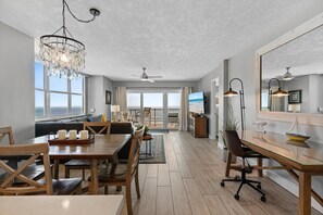 A spacious living area with a dining table, chairs, a chandelier, and a large window overlooking the ocean. - Ponce de Leon Towers 401 (New Smyrna Beach)
