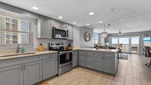 A modern kitchen with grey cabinets, stainless steel appliances, and a large island. - Ponce de Leon Towers 401 (New Smyrna Beach)