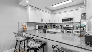 Een moderne keuken met witte kastjes, een groot kookeiland met barstoelen, een magnetron en een fornuis.