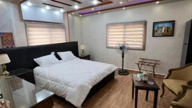 A hotel room with a bed, a desk, a chair, a standing fan, and a window. - PETRA BALCONY APARTMENT (Wadi Musa)