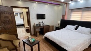 A hotel room with a bed, a desk, a chair, a television, and a decorative wall piece. - PETRA BALCONY APARTMENT (Wadi Musa)
