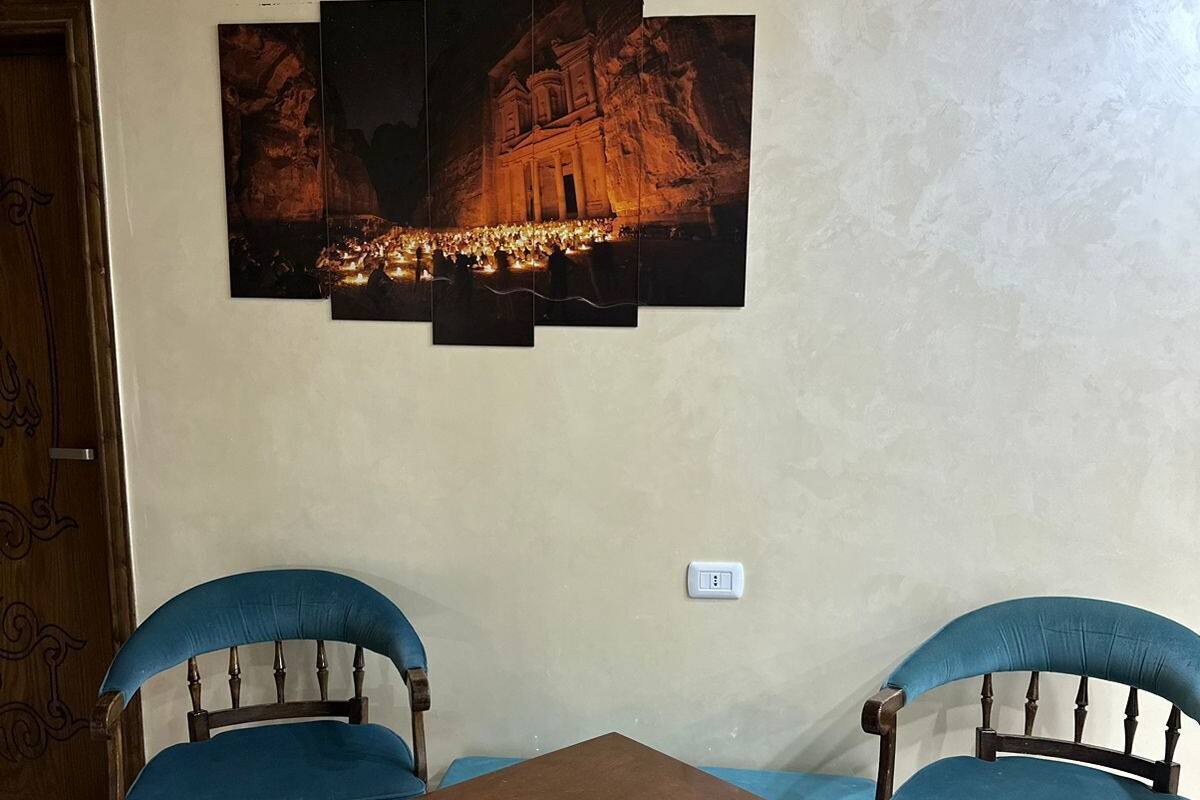 Una stanza con due poltrone rivestite in blu, un tavolino in legno e un'opera d'arte a parete raffigurante un edificio di notte.