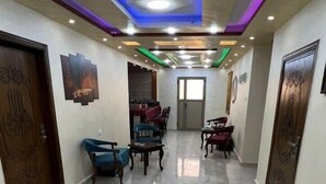 A spacious hallway with a polished marble floor, a dining area with chairs and tables, and a ceiling with recessed lighting and decorative elements. - PETRA BALCONY APARTMENT (Wadi Musa)