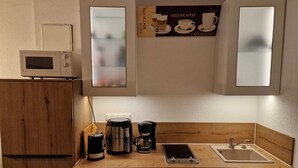 Et kompakt køkken med mikroovn, kaffemaskine og lille vask.