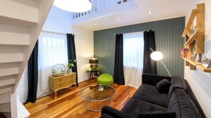 Ein modernes Wohnzimmer mit einem schwarzen Sofa, einem Glastisch, einem Holznachttisch, einem grünen Sessel und einem Bücherregal.