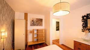 Ein Schlafzimmer mit einem Bett, einem Holzschrank, einem Nachttisch, einem Spiegel und einer Pendelleuchte.