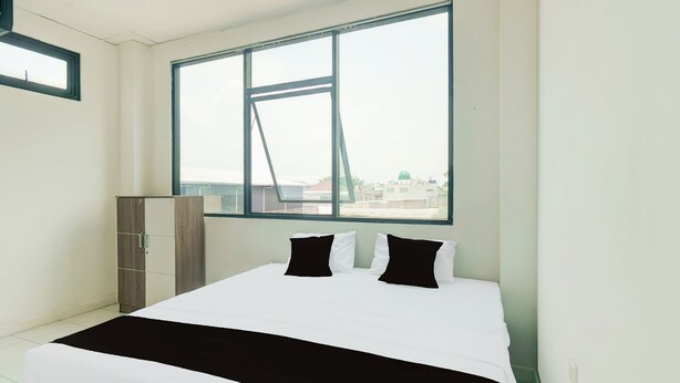 A bedroom with a large window, a bed with black and white bedding, and a wardrobe. - Hotel O Palmerah Near Binus University Formerly Wisma Bango (Jakarta)