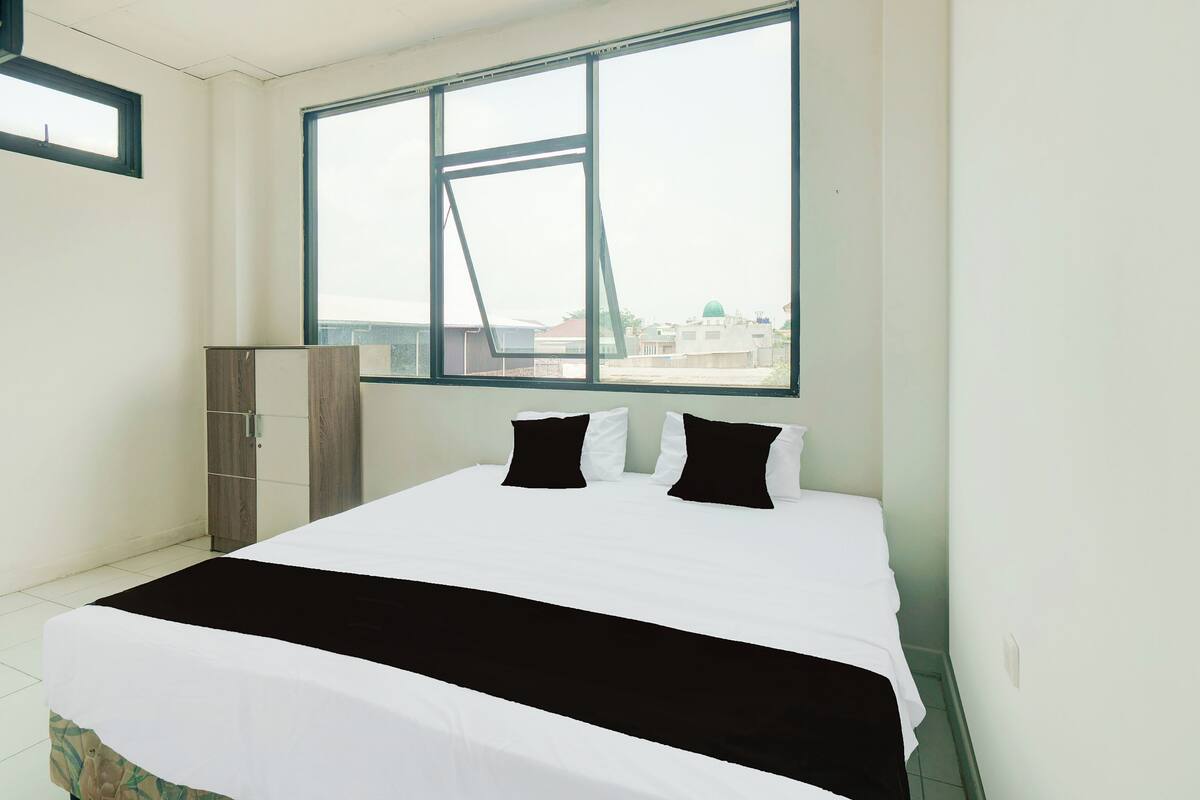 A bedroom with a large window, a bed with black and white bedding, and a wardrobe.