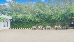 An outdoor seating area with tables and chairs, surrounded by dense greenery and trees. - Hotel O Palmerah Near Binus University Formerly Wisma Bango (Jakarta)