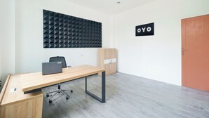 A modern office space with a wooden desk, a laptop, a black acoustic panel, a wardrobe, and a door labeled "OYO". - Hotel O Palmerah Near Binus University Formerly Wisma Bango (Jakarta)