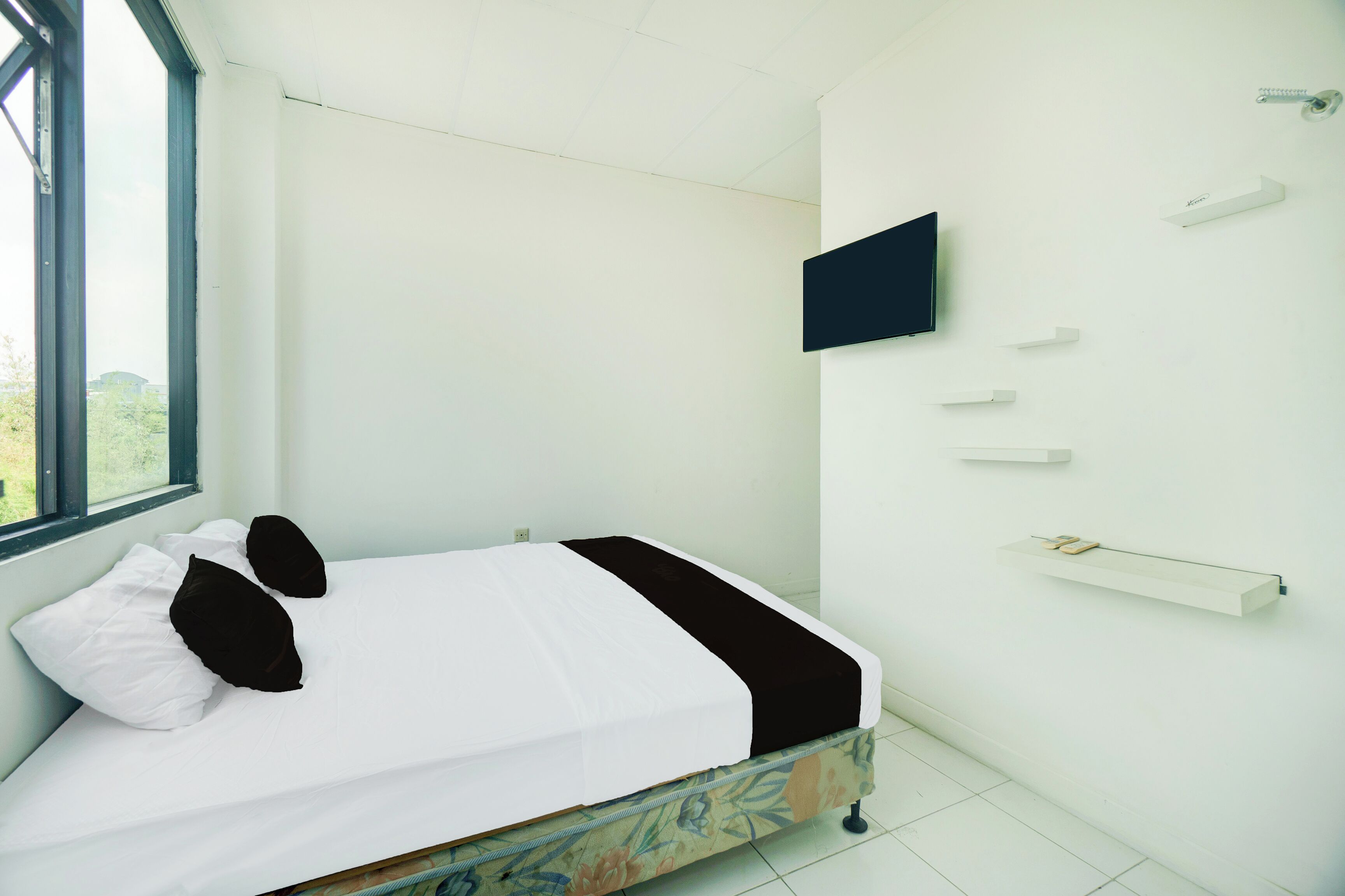 Un dormitorio con una cama, un televisor montado en la pared y una ventana.