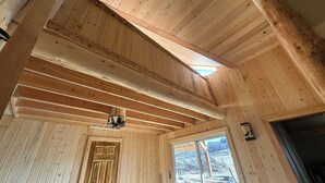 Interior de una cabaña de madera con techo inclinado, una puerta y una ventana con vistas a un espacio exterior.