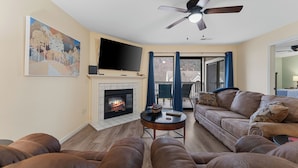 Ein Wohnzimmer mit Kamin, Deckenventilator und großem Fernseher.