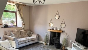 A living room with a sofa, a television, a fireplace, and a window with curtains. - Rustic 2bedroom Cottage With Garden in Sennybridge (Brecon)