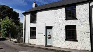A white building with a grey roof, a green door, and a flower wreath on the door. - Rustic 2bedroom Cottage With Garden in Sennybridge (Brecon)