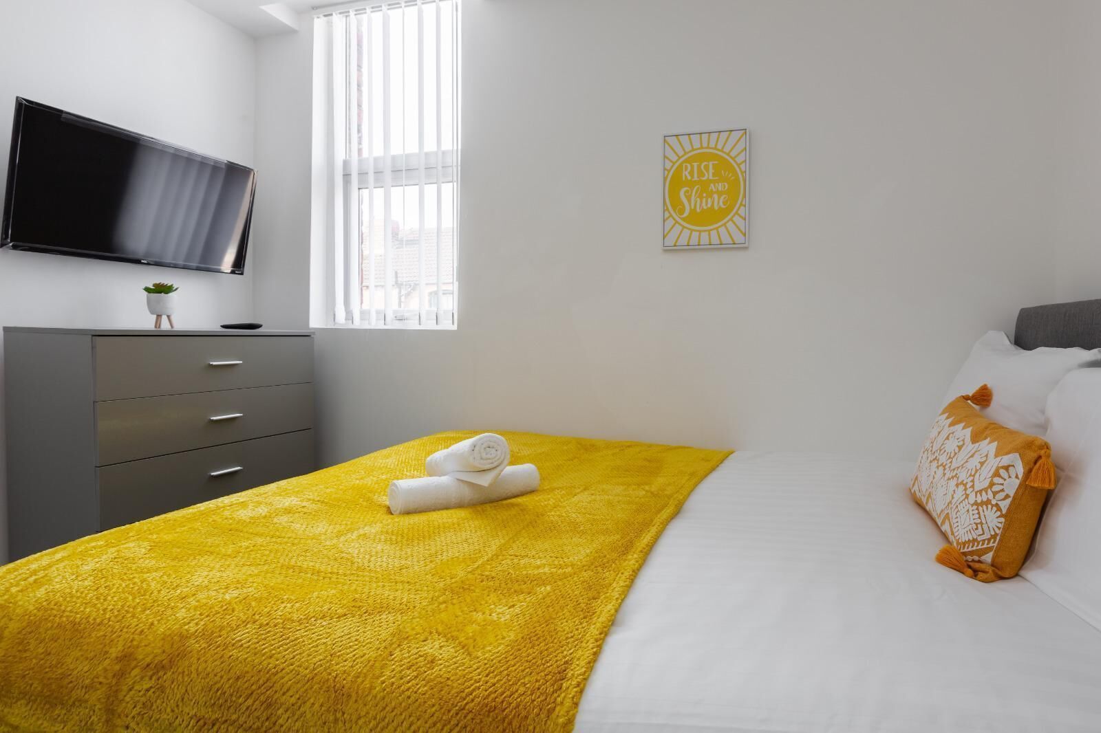 Un dormitorio moderno con cama, televisión, ventana y un cartel motivacional.