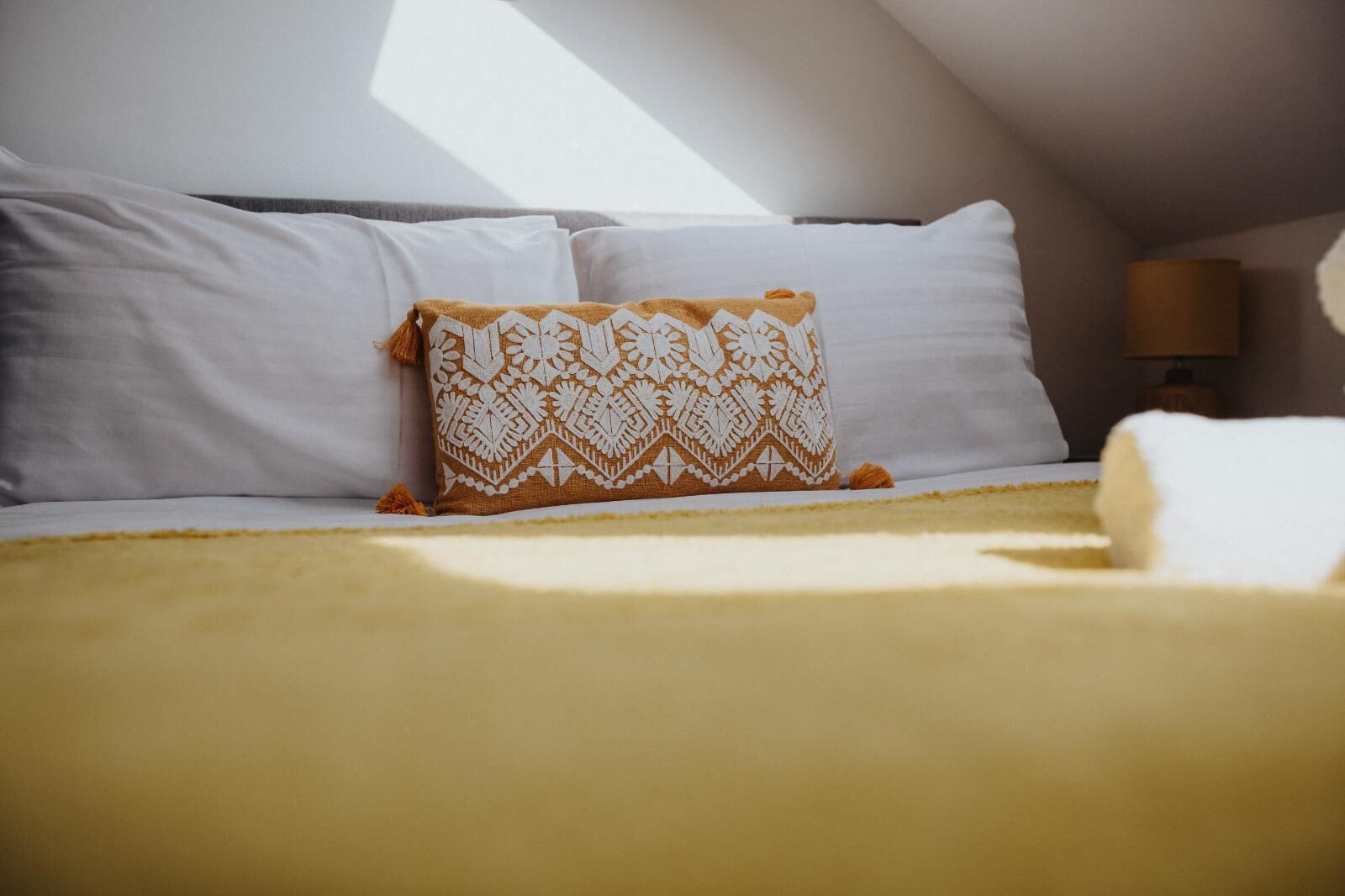 Una cama con almohadas blancas y un edredón estampado, una lámpara y vistas del cielo.