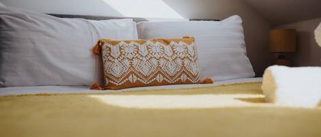 Una cama con almohadas blancas y un edredón estampado, una lámpara y vistas del cielo.