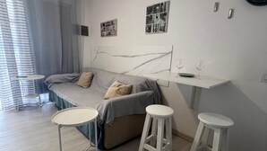 Una sala moderna con un sofá, dos taburetes blancos, una mesita y un ventilador de techo.