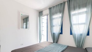 Un dormitorio con cama, ventana con cortinas, espejo y puerta.