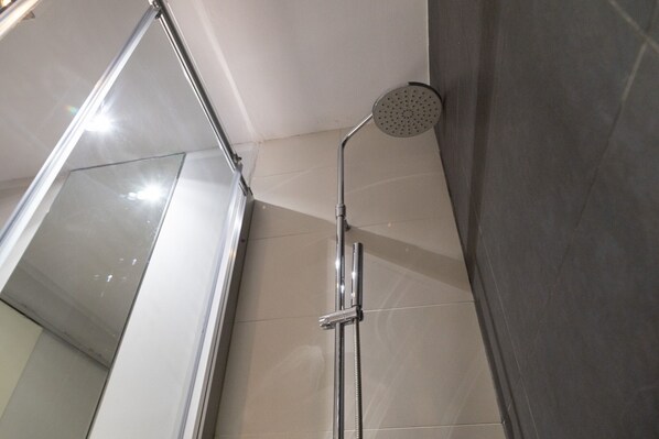Une douche équipée d’un pommeau de douche à main et d’un robinet fixé au mur.