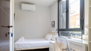 Un dormitorio pequeño y moderno con una cama individual, un escritorio y una ventana.