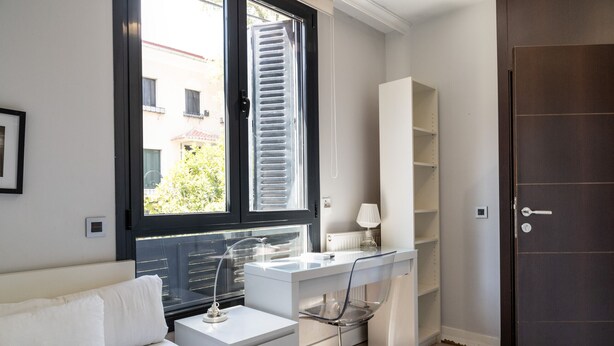 Un dormitorio moderno con cama, escritorio y silla. Hay una ventana con persianas, una puerta y un radiador.